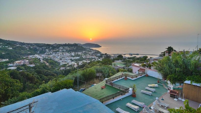 Vista dall'alto sulle terrazze e la piscina della struttura al tramonto, con la baia di Casamicciola