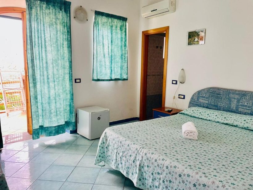 Camera con tende verdi e porta-finestra aperta sulla terrazza vista mare