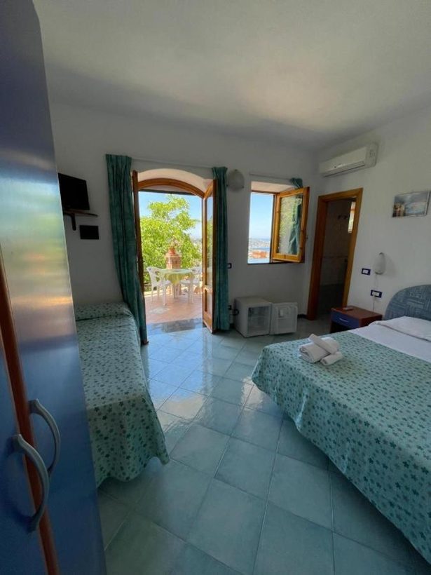 Camera con finestra ad arco che incornicia il mare e pareti in piastrelle azzurre